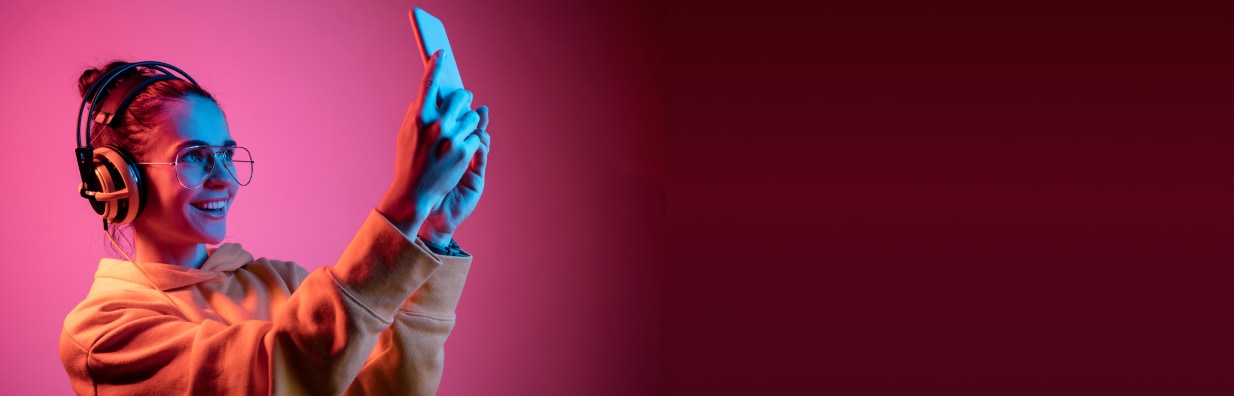 Una donna con cuffie interagisce con un dispositivo mobile, rappresentando l'uso di soluzioni di gaming e realtà estesa per il coinvolgimento del pubblico.